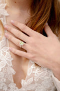 Close up of embroidered Monique Lhuillier Fall 2023 Bliss BL23203 bodice with woman's hand wearing a peridot and diamond radiant cut ring