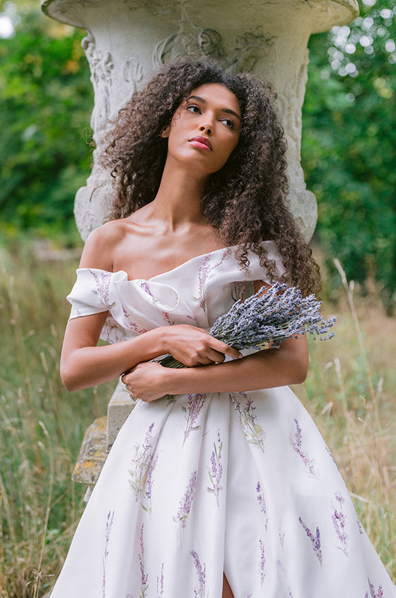 Woman wearing Monique Lhuillier Fall 2023 white and purple off-the-shoulder Lavender floral printed a-line gown