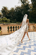 Woman wearing white and multi colored 3D floral Monique Lhuillier Spring 2023 Sicily cocktail dress with Watteau train and matching veil