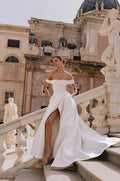 Woman wearing Monique Lhuillier Spring 2023 Bliss white off-the-shoulder mikado a-line BL23109 gown with side slit in skirt
