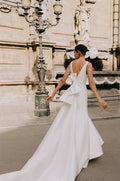 Woman wearing Monique Lhuillier Spring 2023  Bliss white mikado fitted v-neck trumpet BL23107 gown with detachable bow train