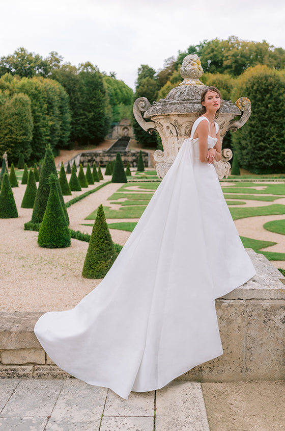 Woman wearing Monique Lhuillier Fall 2023 white strapless mikado Buckingham ballgown with detachable straps and Watteau train