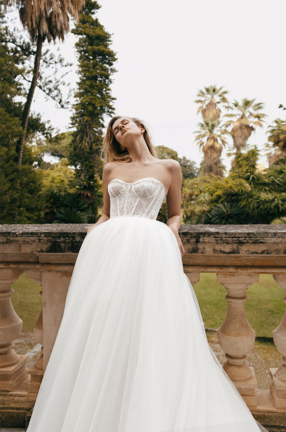 Woman wearing Monique Lhuillier 2023 ivory strapless sweetheart corseted lace and tulle Dorothea ballgown