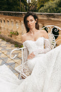 Woman wearing white long sleeve off-the-shoulder mosaic lace Monique Lhuillier Spring 2023 Viviana trumpet gown