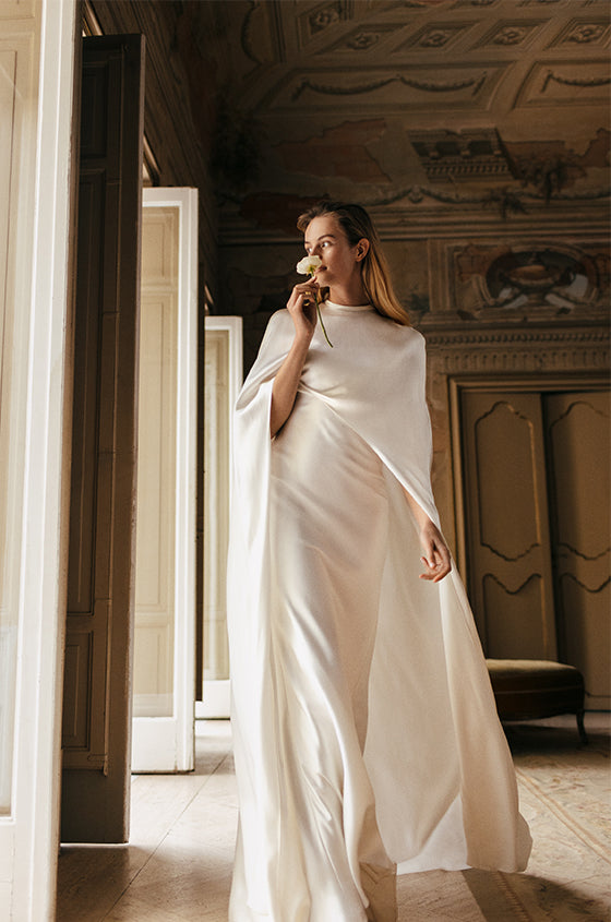 Woman wearing ivory silk charmeuse sheath Monique Lhuillier Spring 2023 Viola gown with matching Viola cape
