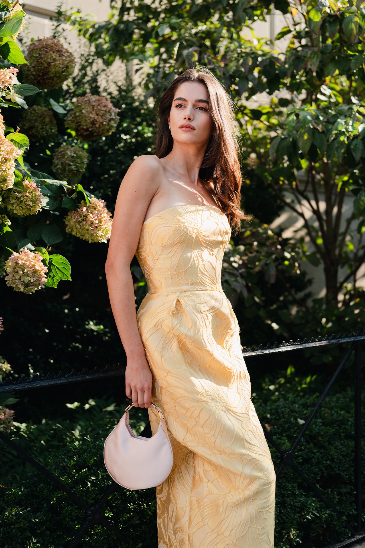 Monique Lhuillier Spring 2025 Strapless, floral jacquard cocktail dress with front pleated skirt and pockets in lemon drop color - lookbook photo on model.