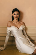 Woman wearing white mikado corseted off-the-shoulder Monique Lhuillier Spring 2023 Marisa cocktail dress with white opera-length gloves