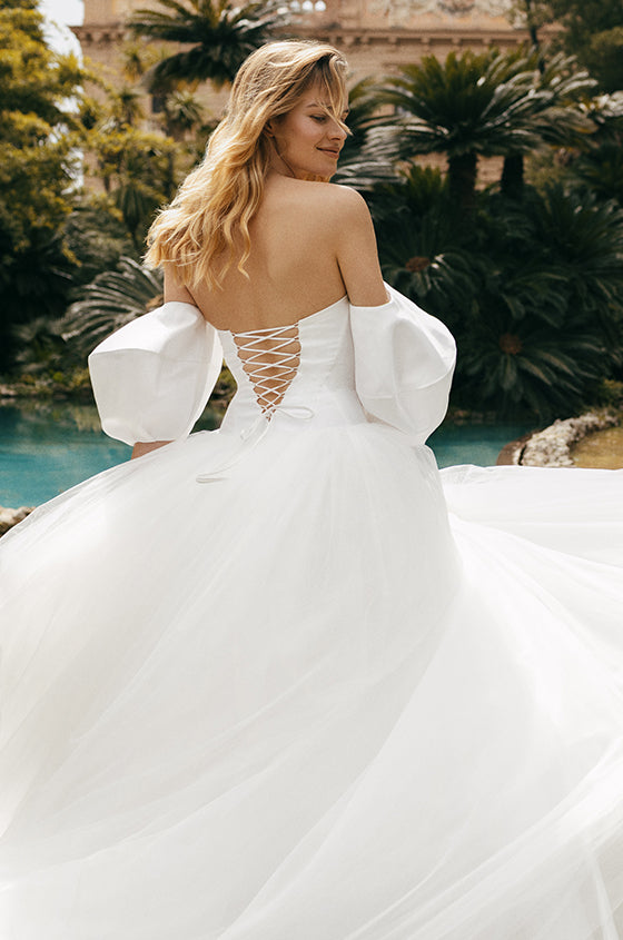 Woman wearing white mikado and tulle Monique Lhuillier Spring 2023 Chiara ballgown with back lace-up corset and tufted sleeves