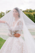 Woman wearing Monique Lhuillier Fall 2023 blush embroidered long-sleeve Marseille ballgown and tulle veil over face