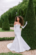 Woman wearing Monique Lhuillier Fall 2023 white mikado Lila trumpet gown with draped bodice and white satin opera length gloves