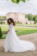 Woman wearing Monique Lhuillier Fall 2023 white lace Elle a-line gown with origami sculpted bodice, tufted sleeves and Watteau train