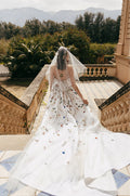 Woman wearing white and multi colored 3D floral Monique Lhuillier Spring 2023 Sicily cocktail dress with Watteau train and matching veil