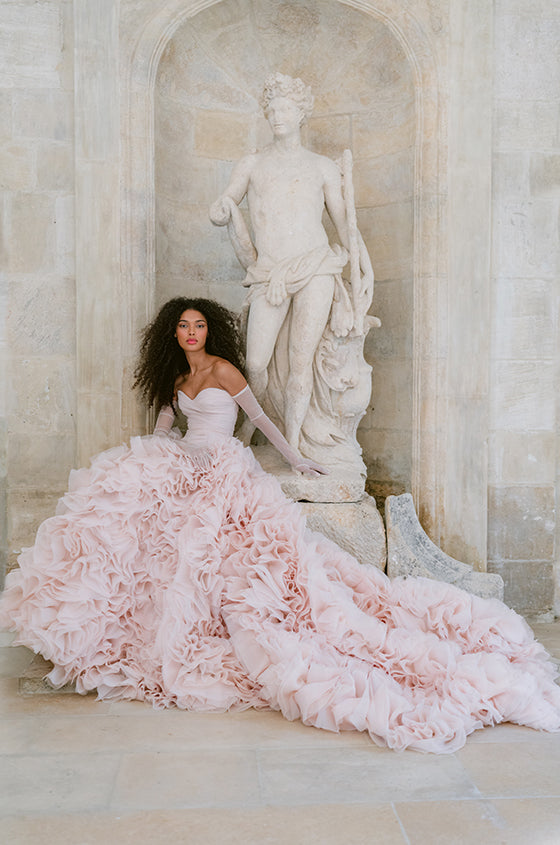 Woman wearing Monique Lhuillier Fall 2023 blush dropped waist Charming ballgown with 3D textured skirt and sheer tulle opera length gloves