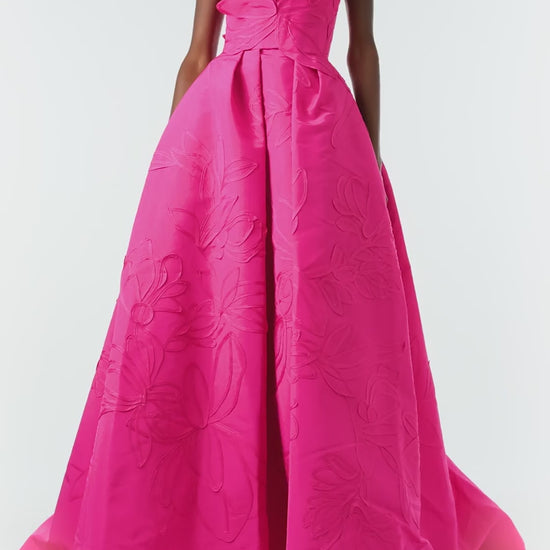 Monique Lhuillier Fall 2024 strapless, a-line ballgown in fuchsia floral embossed faille with draped asymmetrical bodice and full pleated skirt - video.