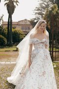 Woman wearing white and multi-colored floral printed off-the-shoulder Monique Lhuillier 2023 Positano ballgown and tulle veil