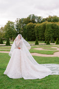 Woman wearing Monique Lhuillier Fall 2023 blush embroidered long-sleeve Marseille ballgown and tulle veil over face