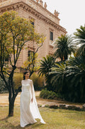 Woman wearing white sequin strapless Monique Lhuillier Spring 2023 Pearla draped column gown with white chiffon Pearla cape