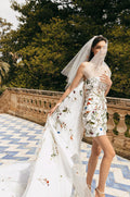 Woman wearing white and multi colored 3D floral Monique Lhuillier Spring 2023 Sicily cocktail dress with Watteau train and matching veil